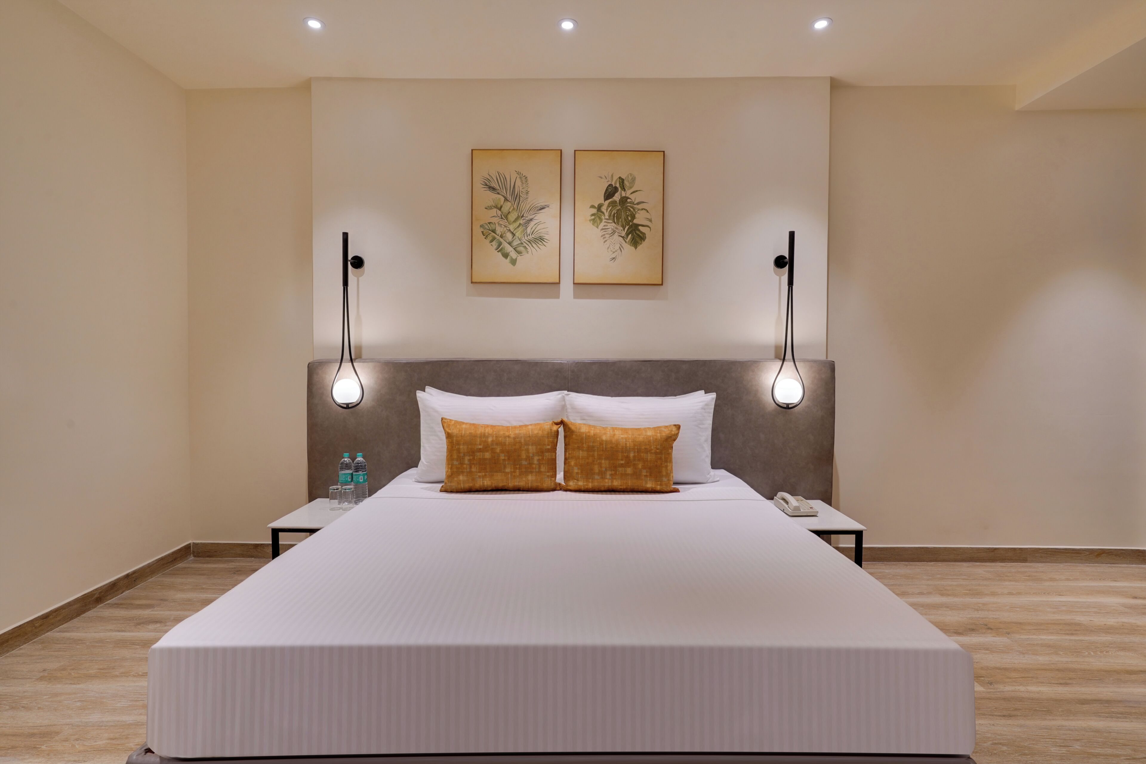 Quarto de hotel com uma cama grande, duas luminárias fixadas na parede e duas gravuras de plantas emolduradas.