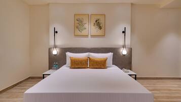 Quarto de hotel com uma cama grande, duas luminárias fixadas na parede e duas gravuras de plantas emolduradas.