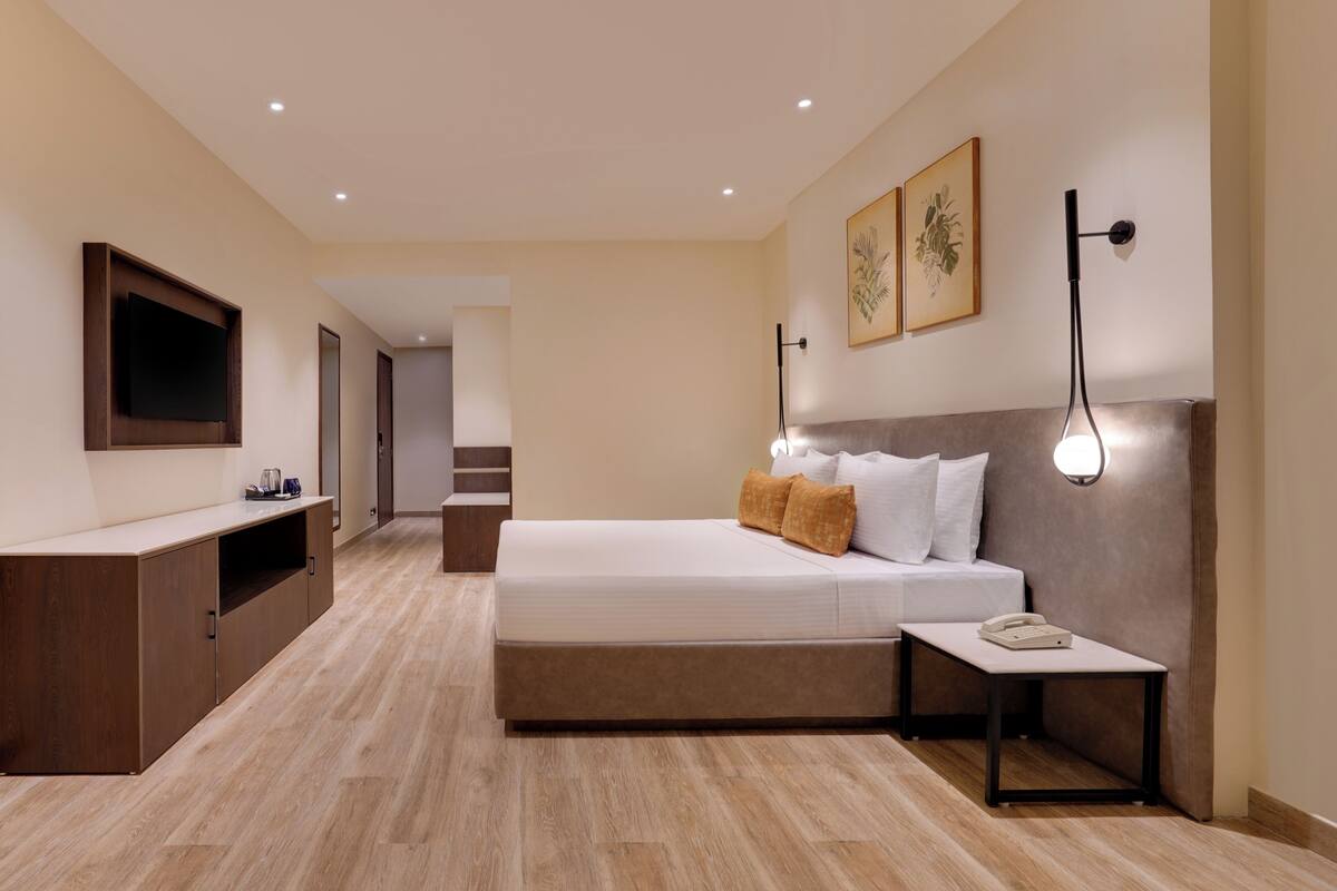Habitación de hotel moderna con una cama grande, mesita de noche y televisor montado en la pared.