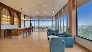 Un moderno vestíbulo de hotel con zona de bar, asientos y grandes ventanales con vistas a la ciudad.