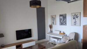 A modern living room with a flat-screen TV, a wooden coffee table, a white piano, and a sofa. - 3* family villa - Walking distance to the lagoon - Heated pool - Saint-Leu (Saint-Leu)