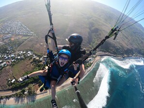 Iemand glijdt in een paraglider over een kustgebied, met uitzicht op een strand en een stad daaronder.