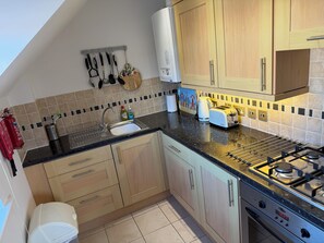 A kitchen with wooden cabinets, a gas stove, a sink, and a toaster. - Ballard Down View, Swanage 2 Bed, 5 minutes walk to beach, balcony views. (Swanage)