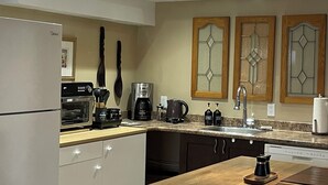 A modern kitchen with a refrigerator, oven, coffee maker, and a wooden dining table.