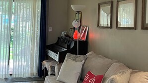 A living room with a sofa, a piano, a lamp, and framed pictures on the wall.