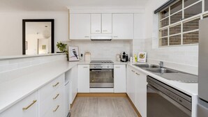 A compact kitchen with white cabinets, a built-in oven, a sink, and a window with a view. - Modern Neutral Haven with Premium Amenities (Griffith)