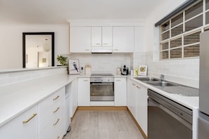 A compact kitchen with white cabinets, a built-in oven, a sink, and a window with a view. - Modern Neutral Haven with Premium Amenities (Griffith)