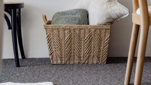 A wicker basket with pillows, a wooden chair, and a small black table against a plain wall. - Modern Neutral Haven with Premium Amenities (Griffith)