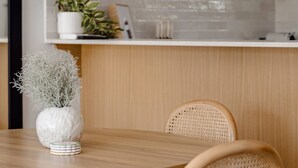 A modern kitchen with white cabinets, a wooden dining table, and a potted plant. - Modern Neutral Haven with Premium Amenities (Griffith)