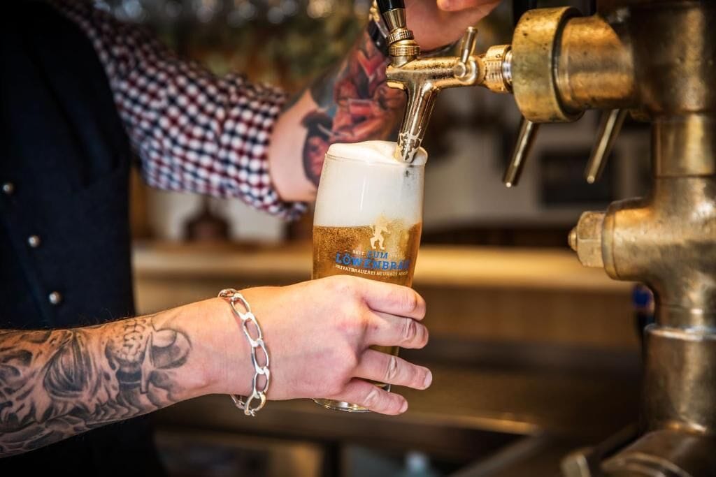 Une personne tenant un verre avec un robinet à bière et une étiquette indiquant « Lowenbrau ».