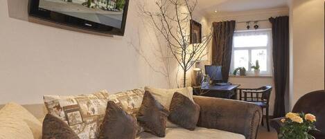 A living room with a sofa, a television mounted on the wall, a lamp, and a window with curtains.