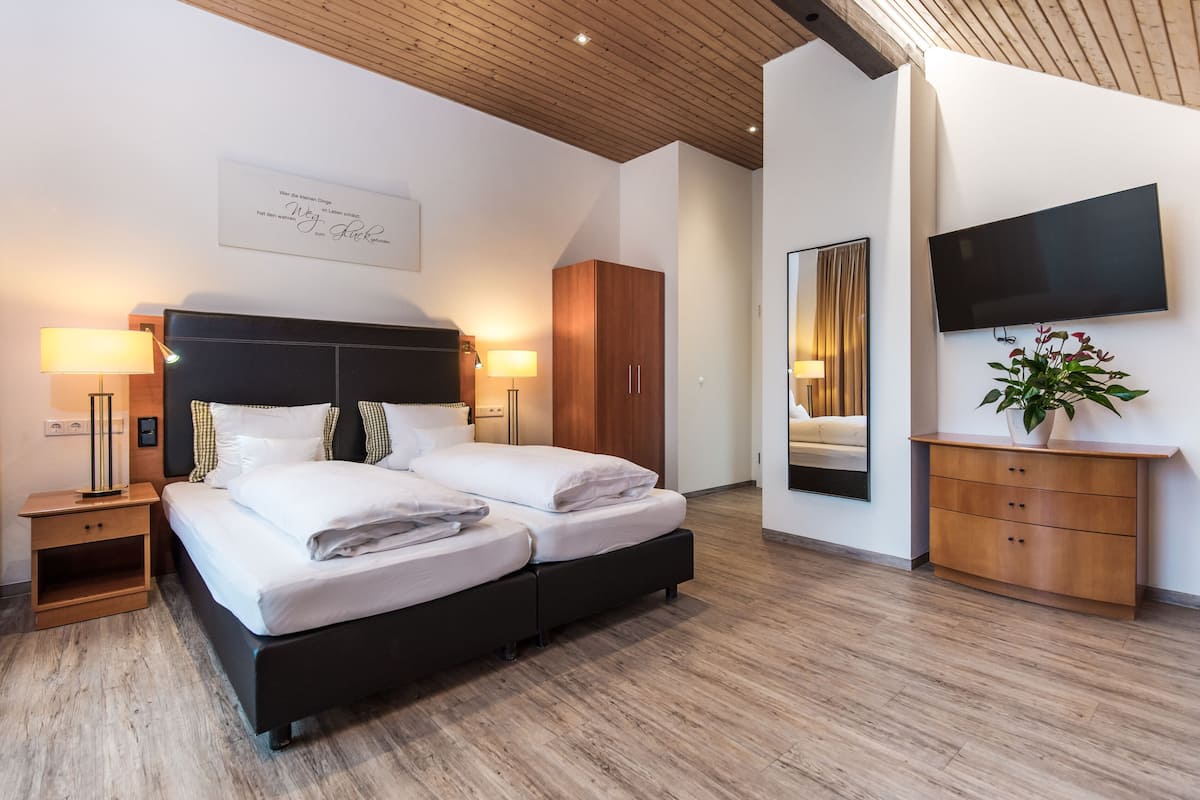 Una habitación de hotel moderna con una cama doble, lámparas de noche, un cabecero de madera, un televisor, un espejo y un armario de madera.