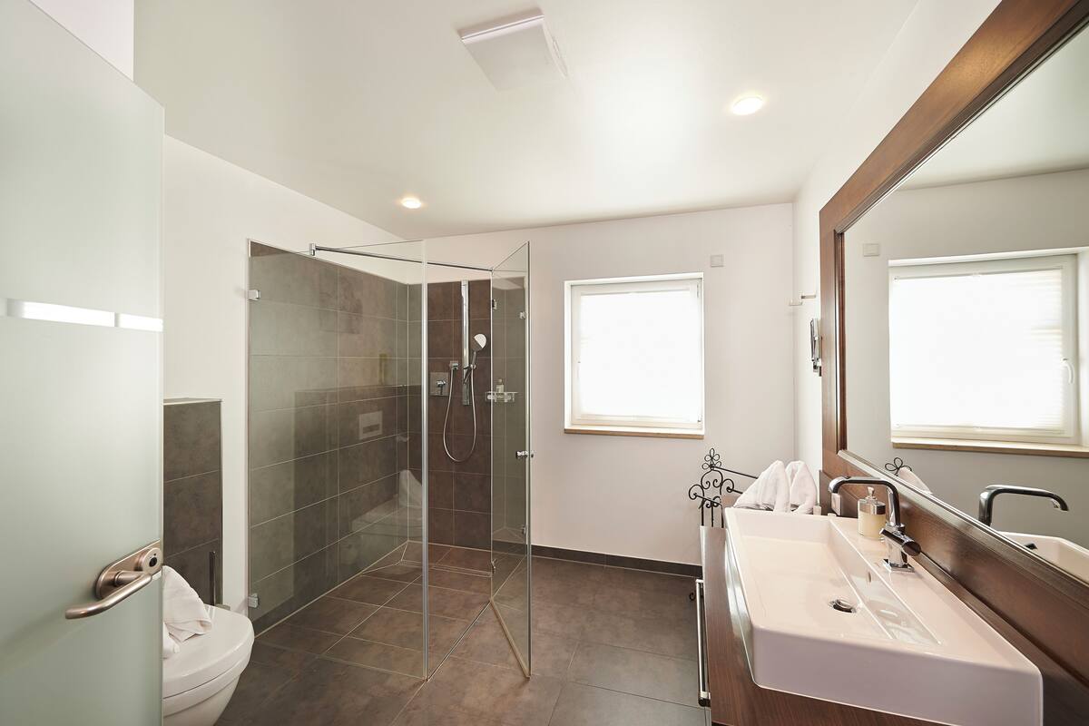 Un baño moderno con cabina de ducha de vidrio, lavamanos blanco y un espejo grande.