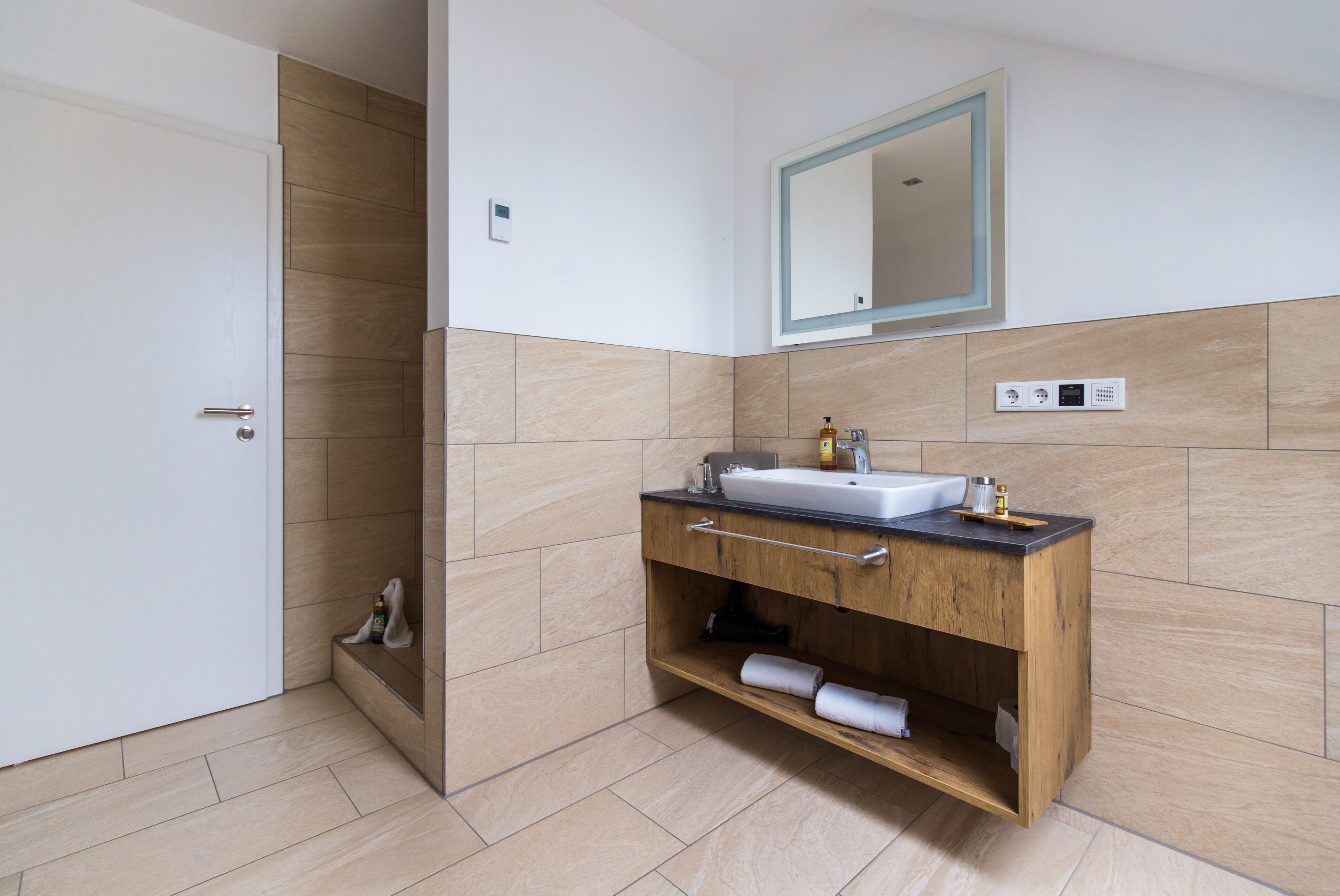 A modern bathroom with a wooden vanity, a white sink, and a mirror.
