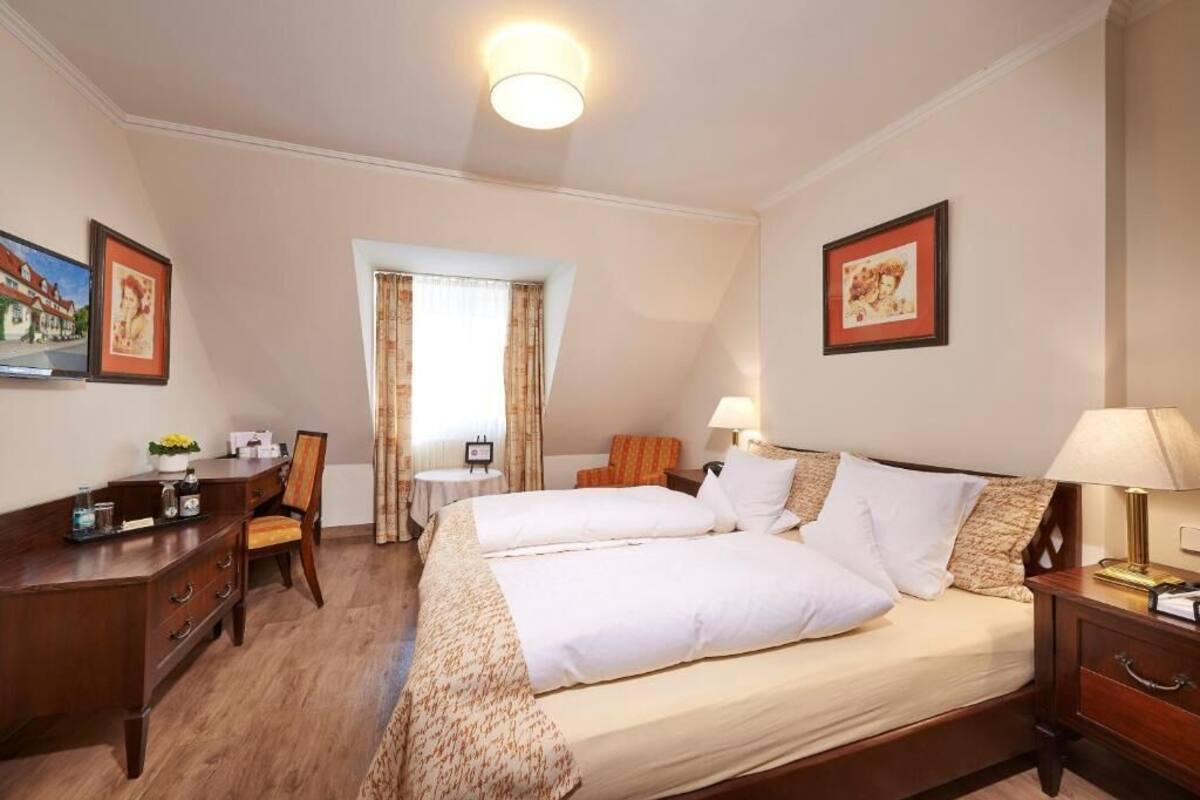 Habitación de hotel con cama, escritorio, silla, mesita y ventana con cortinas.