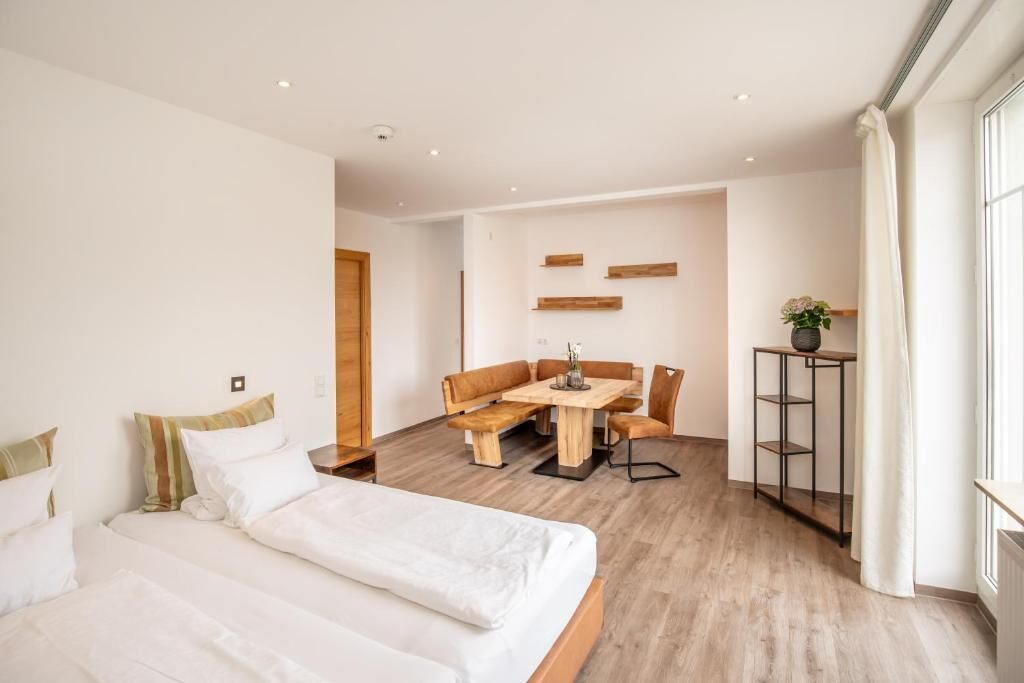 A modern hotel room with a large bed, a wooden dining table, and a small seating area.