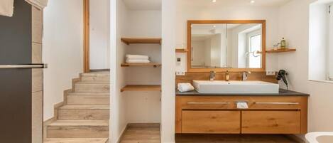 Un baño moderno con tocador de madera, un espejo grande y una escalera que conduce a otra habitación.