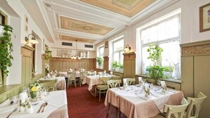 Un comedor con mesas dispuestas para el servicio, un techo decorativo y ventanas amplias con plantas.