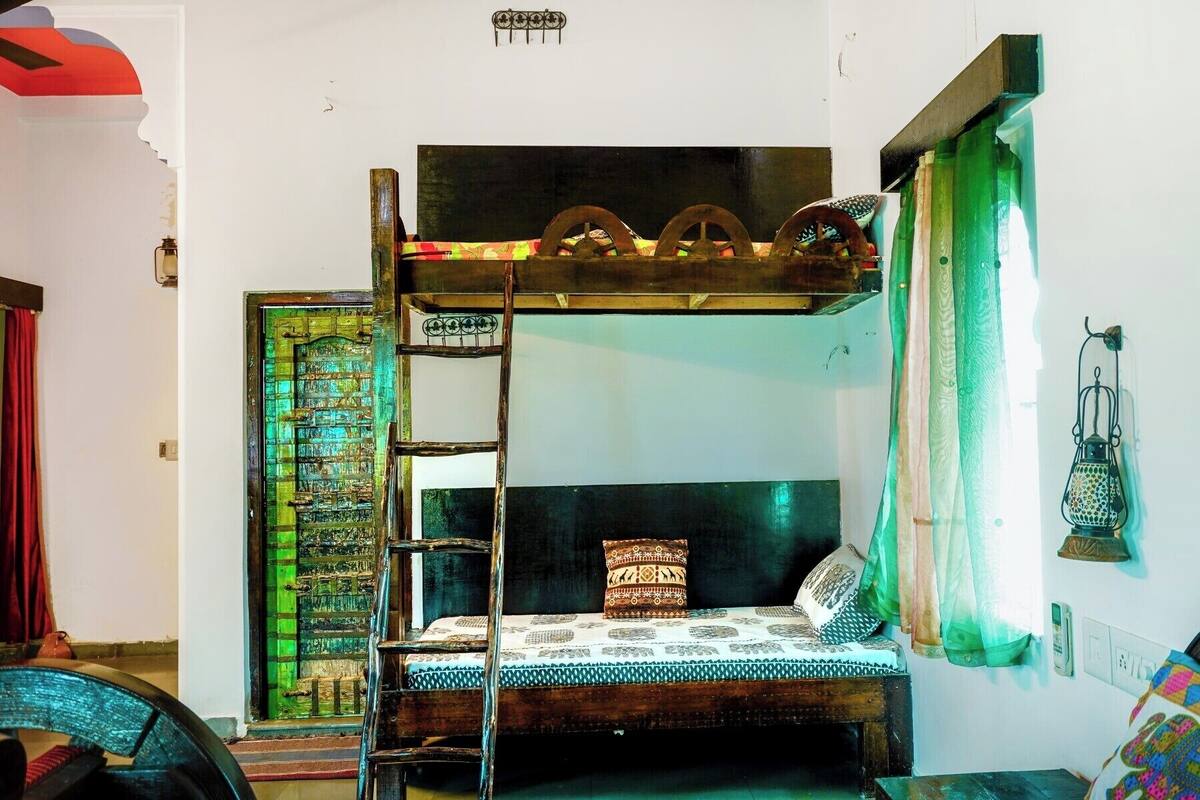 Een stapelbed met een ladder, een groene deur en een raam met gordijnen.