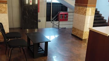A lobby with a reception desk, a staircase, and a seating area with chairs.