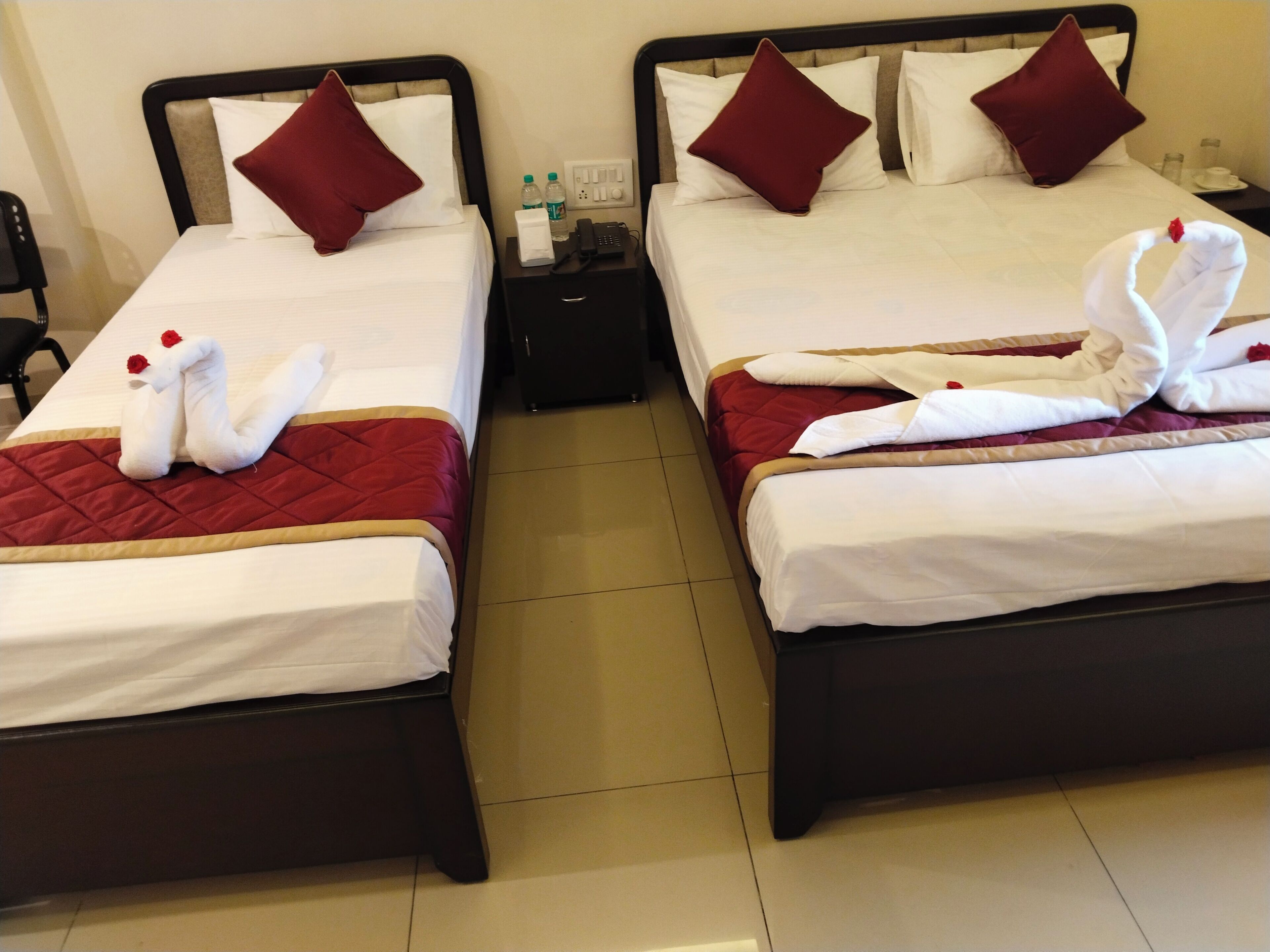 Two twin beds with red and white bedding, a nightstand with a phone and water bottles, and decorative swan towels.
