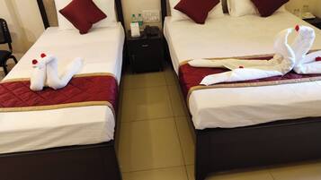 Two twin beds with red and white bedding, a nightstand with a phone and water bottles, and decorative swan towels.