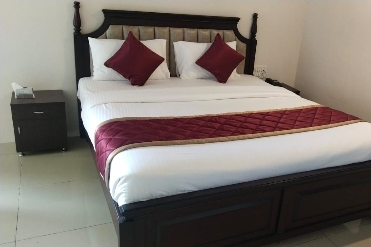 A neatly made bed with a wooden headboard, a bedside table with a lamp, and a red quilted blanket.