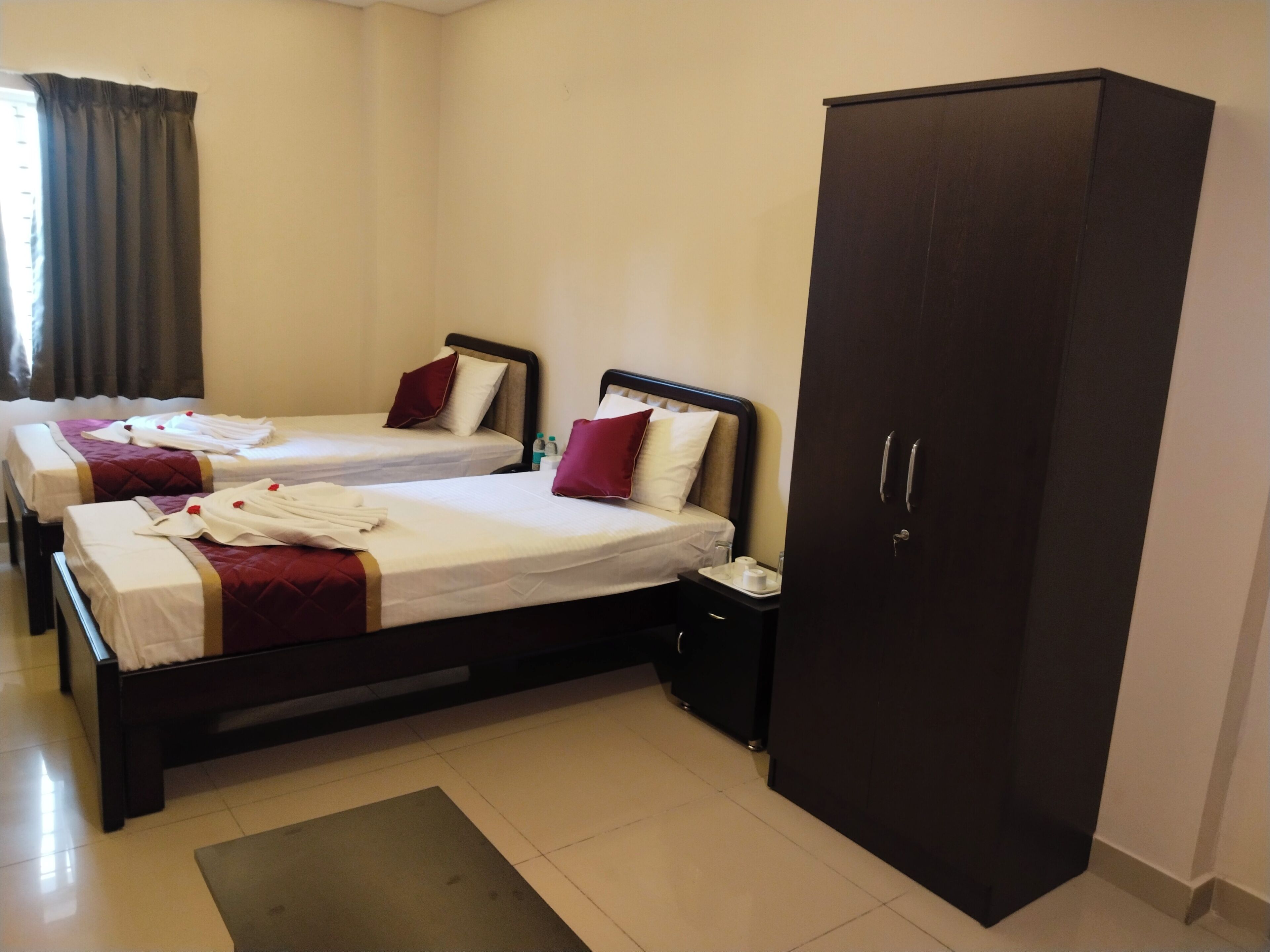 A hotel room with two beds, a wardrobe, and a small bedside table.