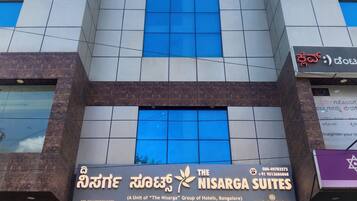 A hotel building with multiple windows and a sign for 'The Nisarga Suites.'