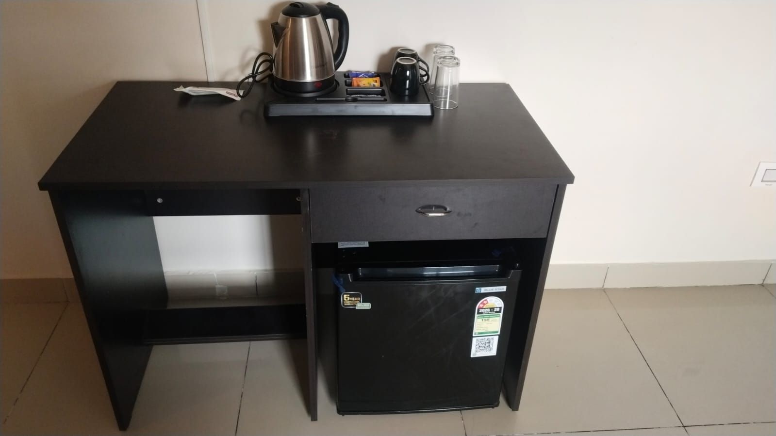 A compact kitchenette with a black refrigerator, a kettle, and a coffee maker on a dark countertop.