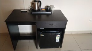 A compact kitchenette with a black refrigerator, a kettle, and a coffee maker on a dark countertop.