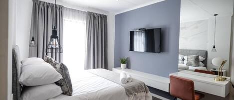 Una camera d'albergo moderna con un letto, una scrivania e una sedia, una TV a parete e una finestra con tende.