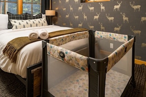 Ein Hotelzimmer mit Bett, Fenster, Lampe und Babybett.