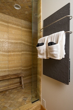 Ein Badezimmer mit Duschkabine aus Glas, einer Holzbank und einem Handtuchhalter mit zwei Handtüchern.