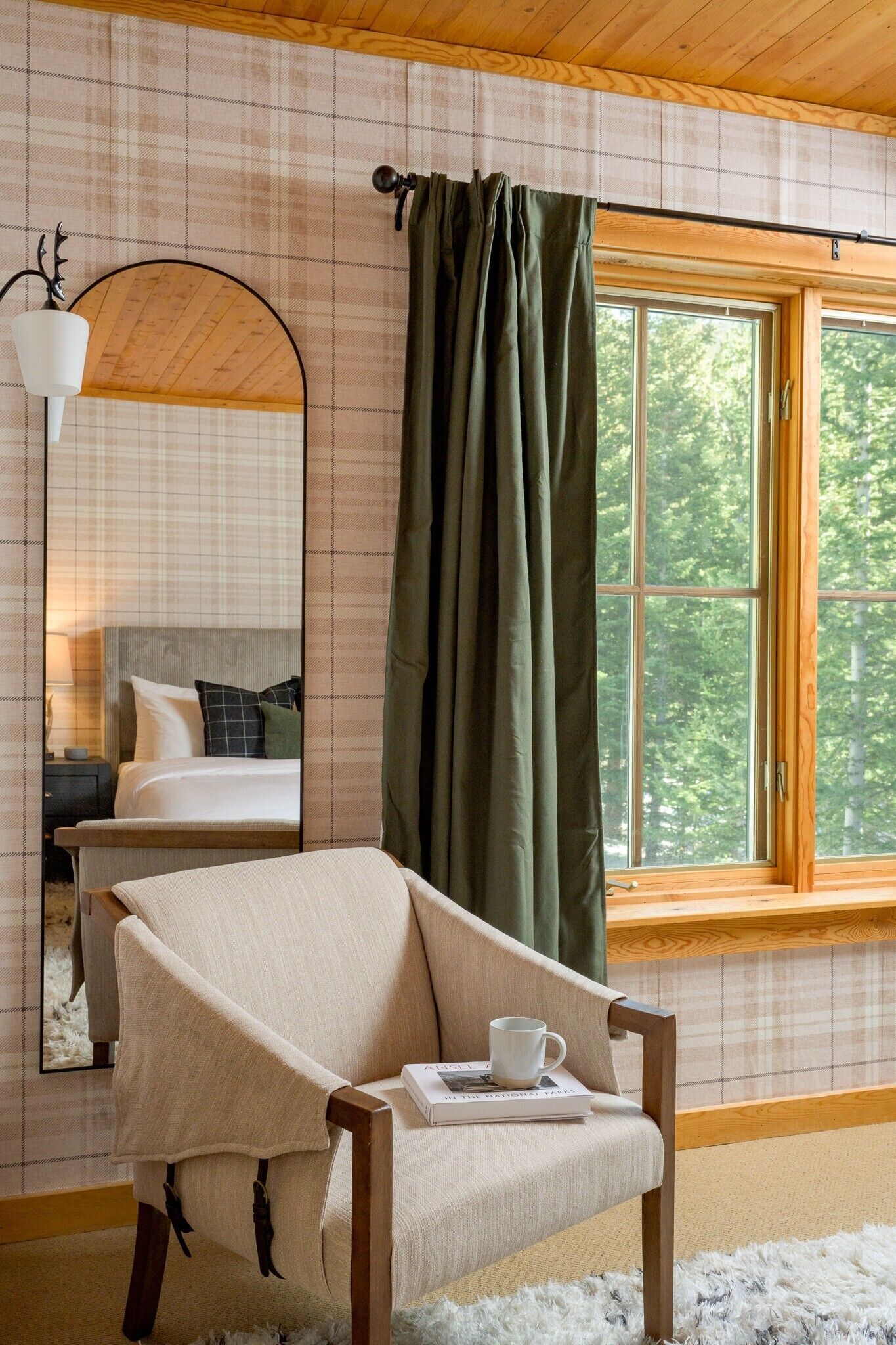 A room with a bed, a chair, a window with curtains, a lamp, and a mirror.