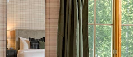 A room with a bed, a chair, a window with curtains, a lamp, and a mirror.