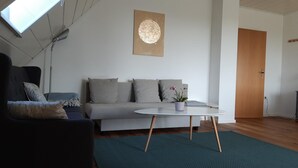 Ein modernes Wohnzimmer mit einer Couch, einem Couchtisch, einer Zimmerpflanze und einem an der Wand befestigten Kunstwerk.