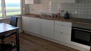 Eine Küche mit weißen Schränken, einer Holz Arbeitsplatte, einem Spülbecken, einem Herd und einem Fenster mit Blick auf ein Feld.