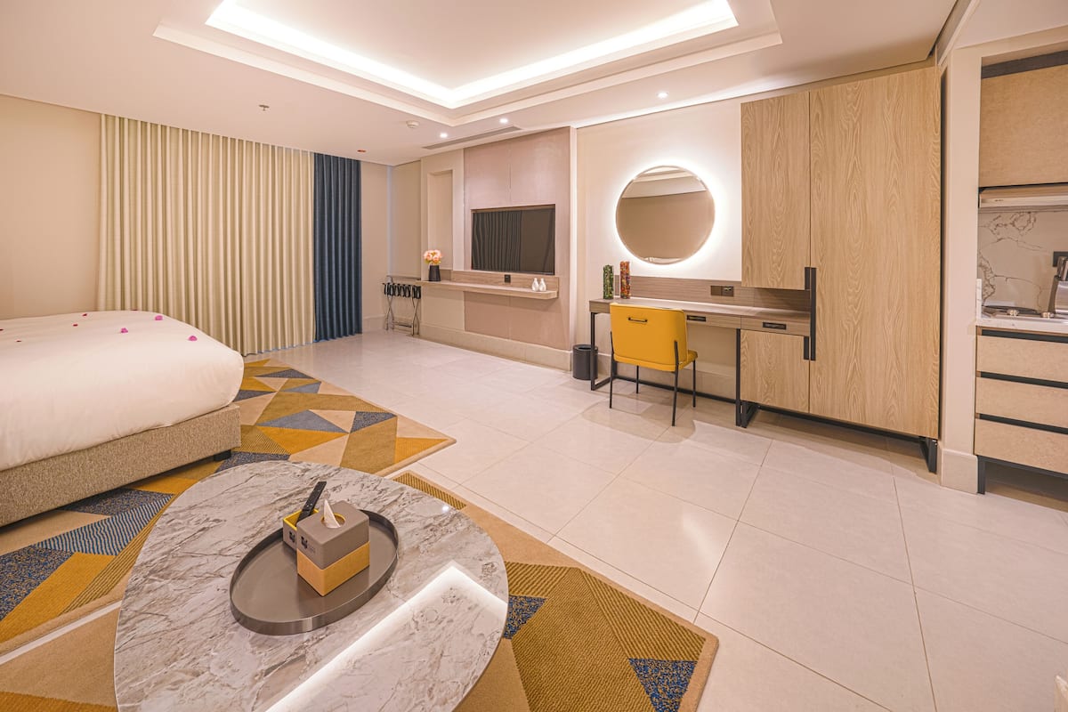 A modern hotel room with a bed, a desk, a round mirror, and a TV.