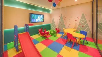 A children's play area with a slide, play structures, and a television screen.