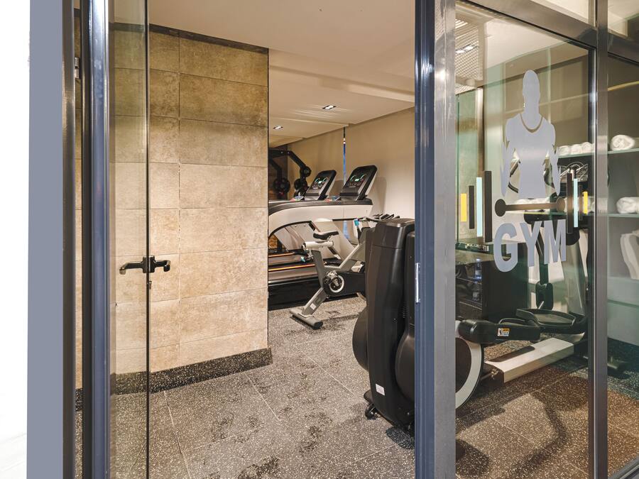 Un gimnasio con equipo de ejercicio, una entrada con puerta de vidrio y suelo de baldosas.