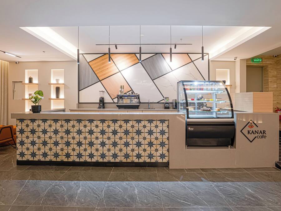 A modern reception desk with a coffee machine, a glass display case, and a patterned tile wall.