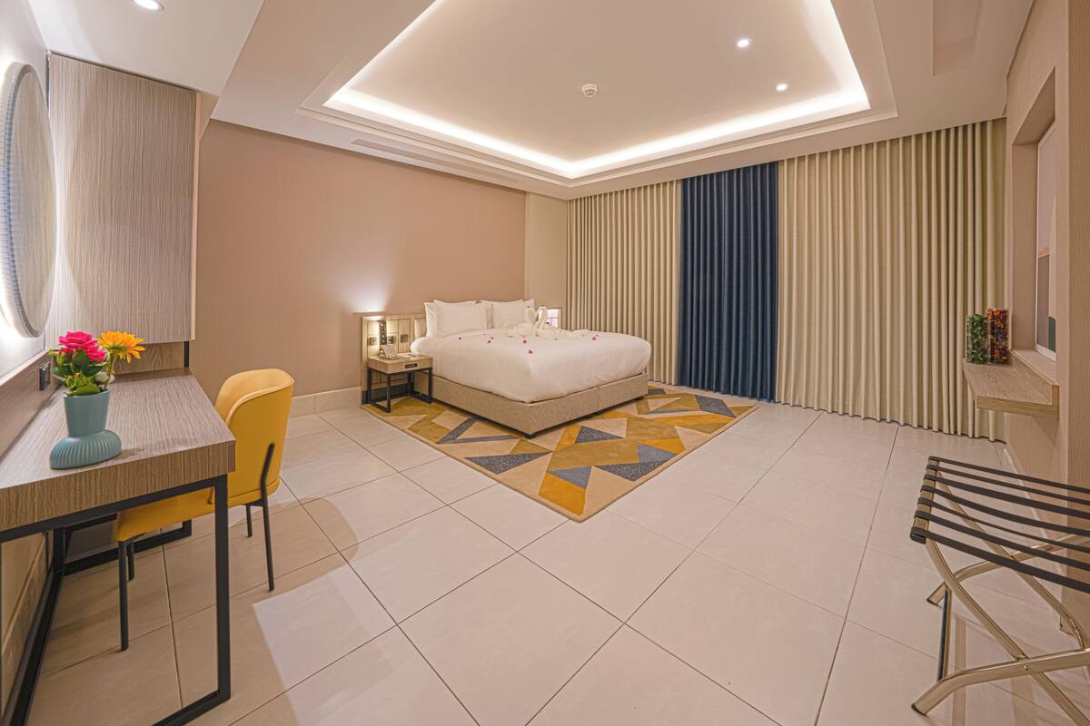A modern hotel room with a bed, bedside table, chair, desk, and a decorative rug.