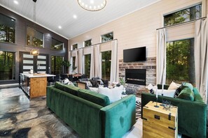 Ein modernes Wohnzimmer mit Kamin aus Naturstein, grünen Sofas und einem Flachbildfernseher.