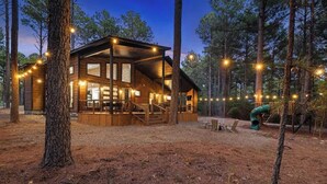Una cabaña de madera con ventanas grandes, una terraza y luces colgantes.