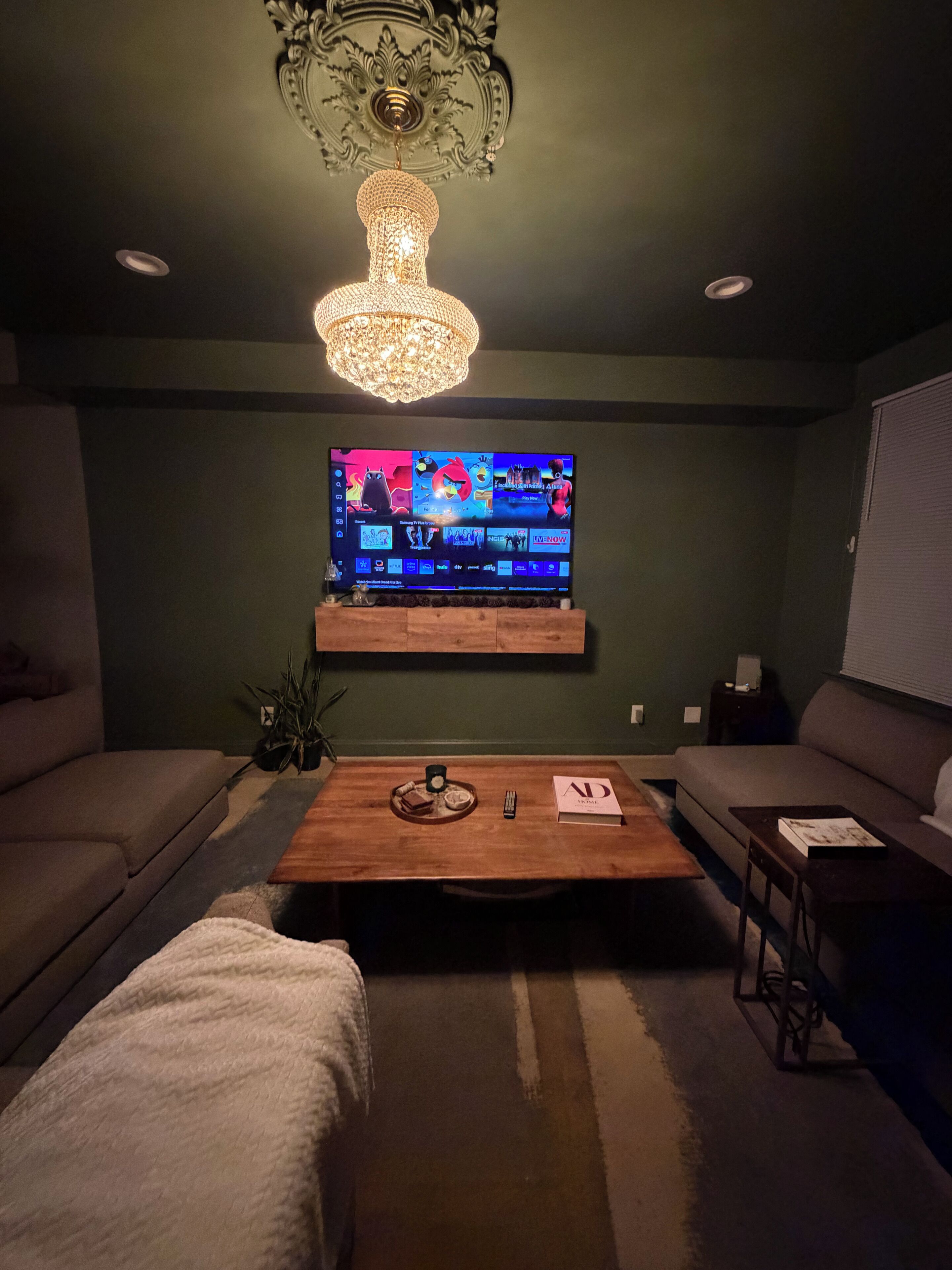A living room with a flat-screen TV, a wooden coffee table, a sofa, and a chandelier.