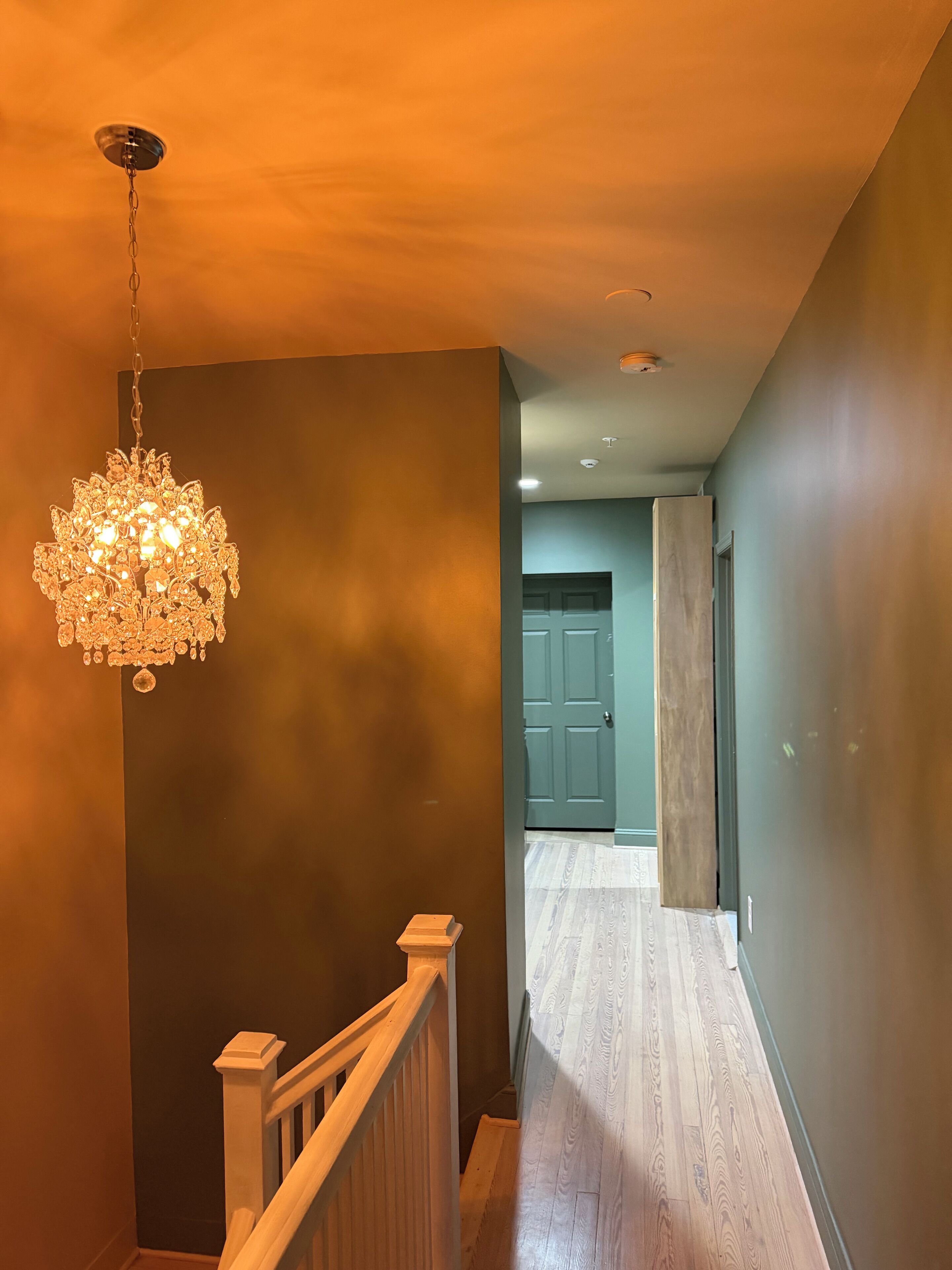 A staircase with a wooden handrail and a hanging chandelier.