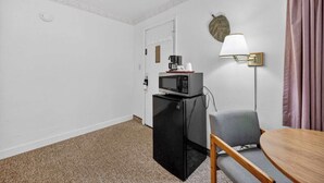 A compact room with a kitchenette, a microwave, a refrigerator, a small table, a chair, and a wall-mounted lamp. - Eagle Motel Suite 100 (Manitou Springs)