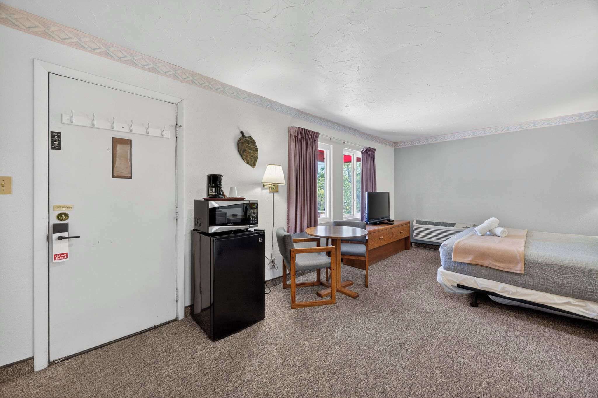 A compact room with a bed, a desk with a computer, a refrigerator, and a television.