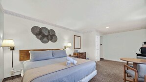 A hotel room with a bed, bedside lamps, a desk, and a chair. - Eagle Motel Suite 100 (Manitou Springs)